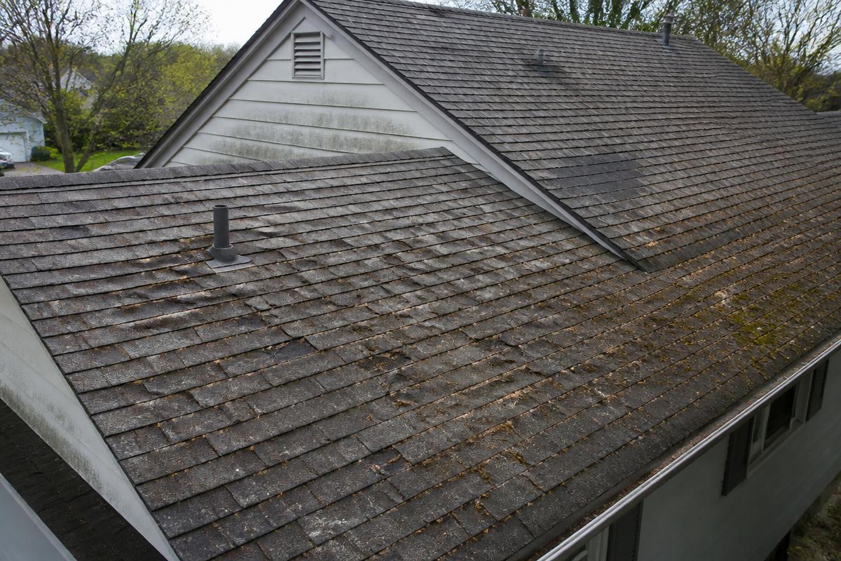 Worn asphalt shingle roof with curling shingles and moss growth